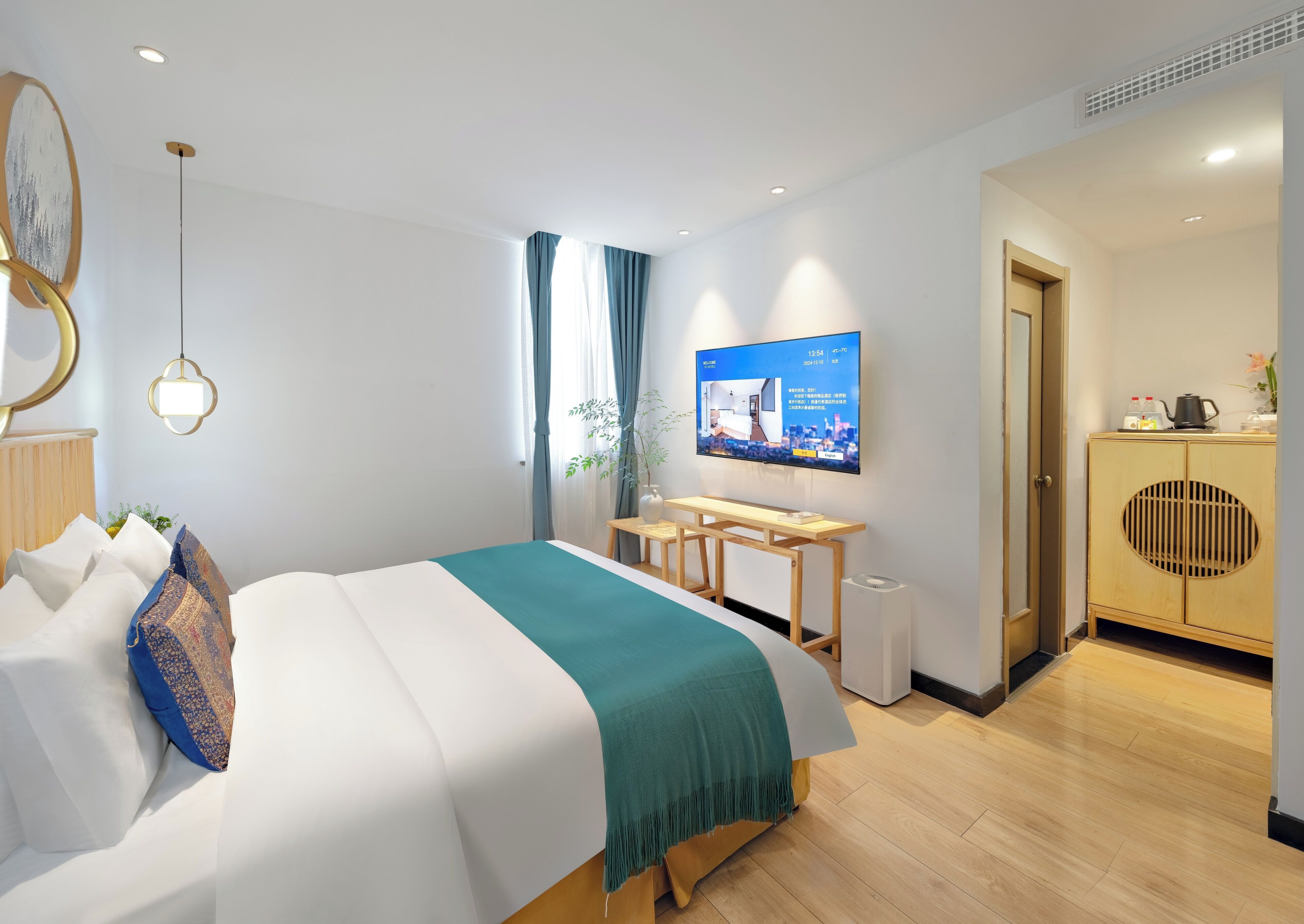 A modern hotel room with a bed, a desk, a television, and a wardrobe.