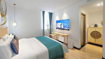 A modern hotel room with a bed, a desk, a television, and a wardrobe.