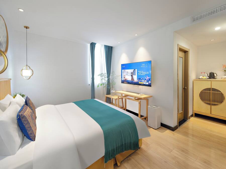 A modern hotel room with a bed, a desk, a television, and a wardrobe.