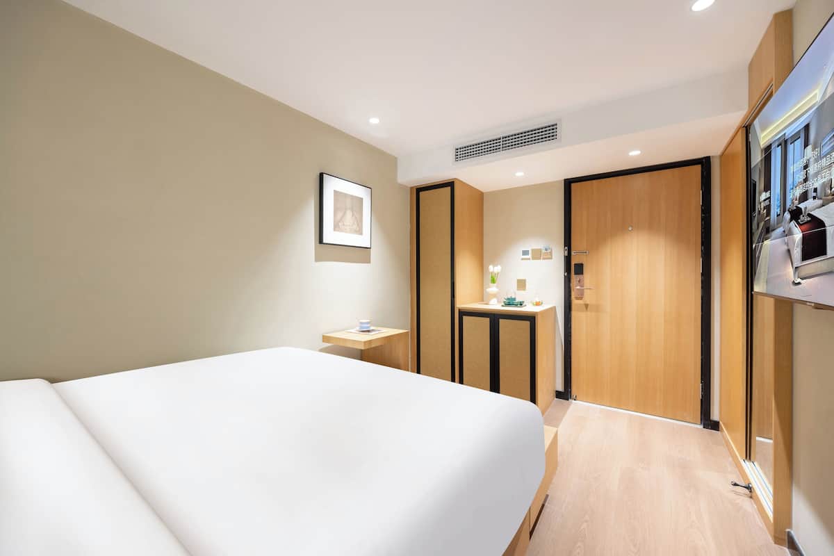 Une chambre d’hôtel avec un grand lit, une petite table de chevet, un miroir, une armoire et un téléviseur.