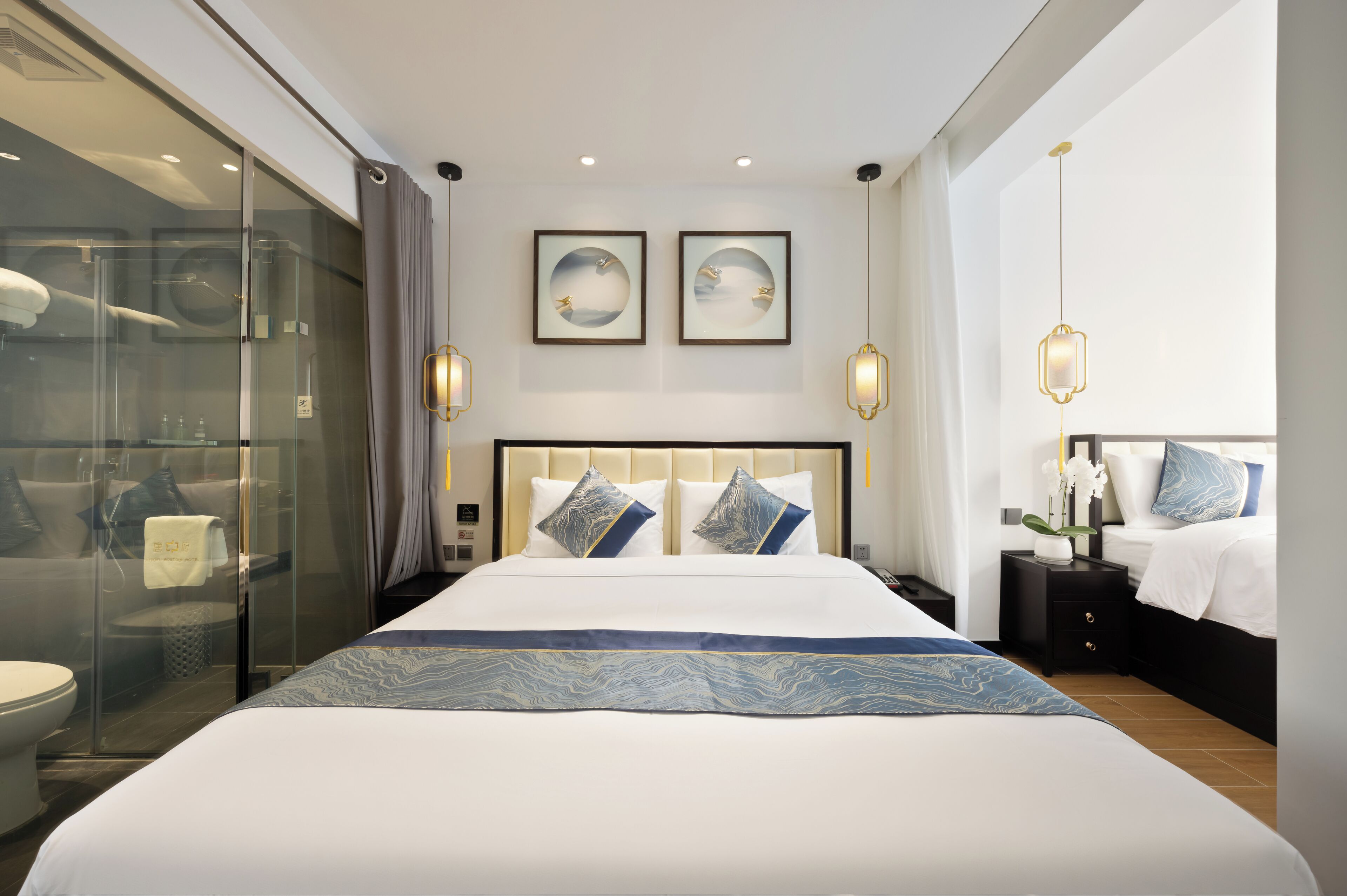 A modern hotel room with a large bed, a glass shower enclosure, and two wall-mounted picture frames.
