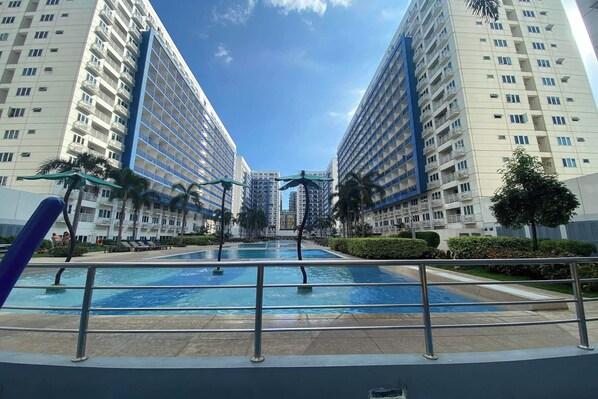 A modern hotel with a central swimming pool, surrounded by high-rise buildings and palm trees. - Madison's Place at Sea MOA (Pasay)
