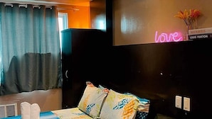 A modern hotel room with a bed, a black leather sofa, and a neon sign on the wall. - Madison's Place at Sea MOA (Pasay)