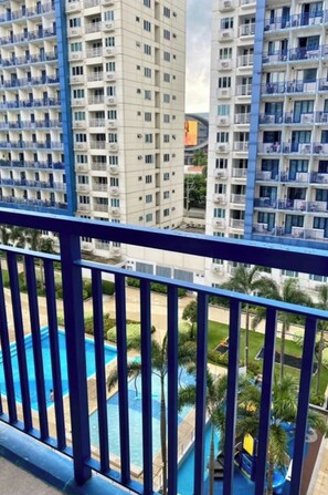 A high-rise building with multiple balconies, a swimming pool, and surrounding greenery. - Madison's Place at Sea MOA (Pasay)