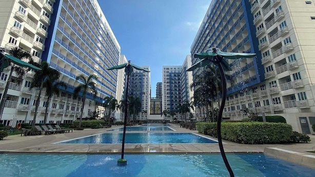A swimming pool with two water jets in the center, surrounded by high-rise buildings with balconies. - Madison's Place at Sea MOA (Pasay)