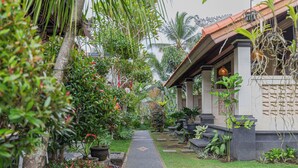 A pathway leading to a building with a tiled roof and columns, surrounded by lush greenery and potted plants. - Campuhan Guesthouse (Penebel)