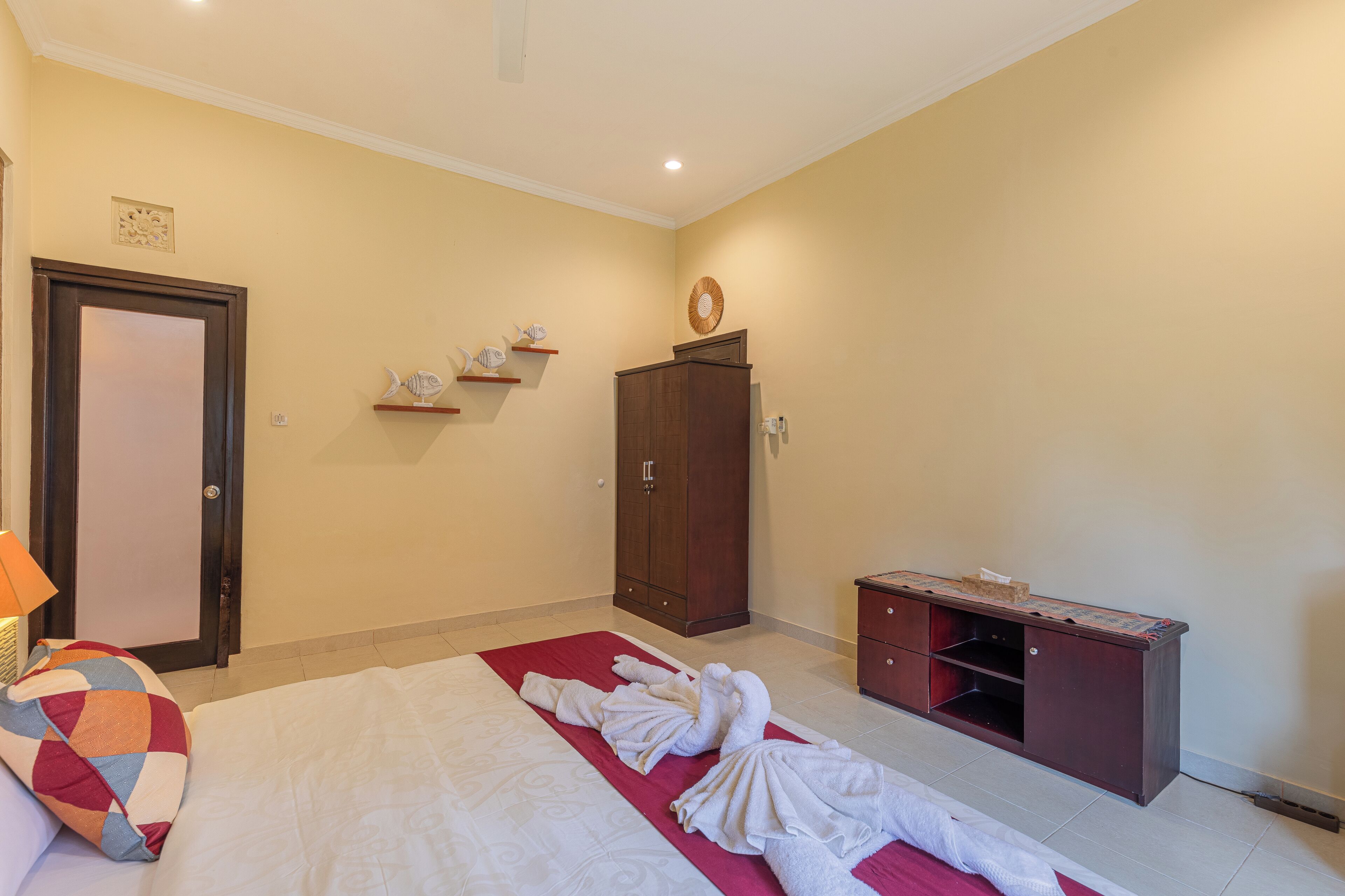 A hotel room with a bed, a wooden cabinet, a small shelf with decorative items, and a door.