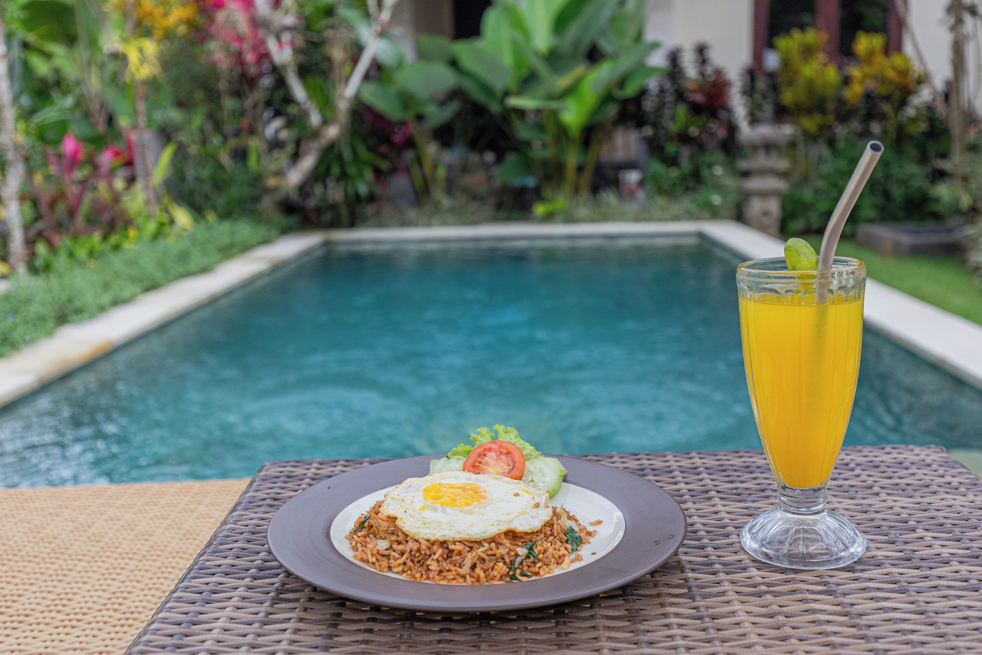 Une table à manger avec une assiette de riz frit aux œufs, un verre de jus d’orange et une paille.