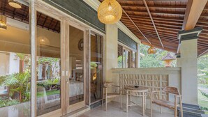 A covered outdoor seating area with wooden furniture and a view of a garden. - Campuhan Guesthouse (Penebel)