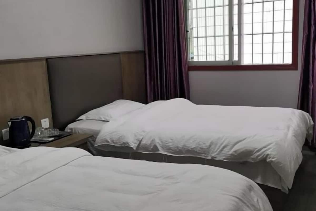 A hotel room with two beds, a nightstand with a kettle, and a window with curtains.