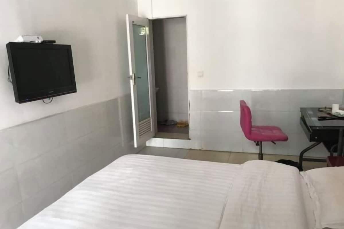 A hotel room with a bed, a desk, a chair, and a television mounted on the wall.