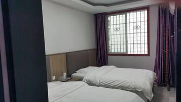 Una habitación de hotel con dos camas, un ventanal con cortinas y una mesita de noche con lámpara.