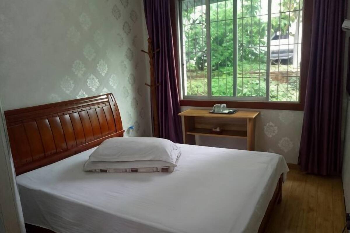 A neatly made bed with a wooden headboard, a bedside table with a lamp, and a window with curtains.