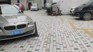 Un estacionamiento con un coche BMW, un scooter rojo y una furgoneta blanca.