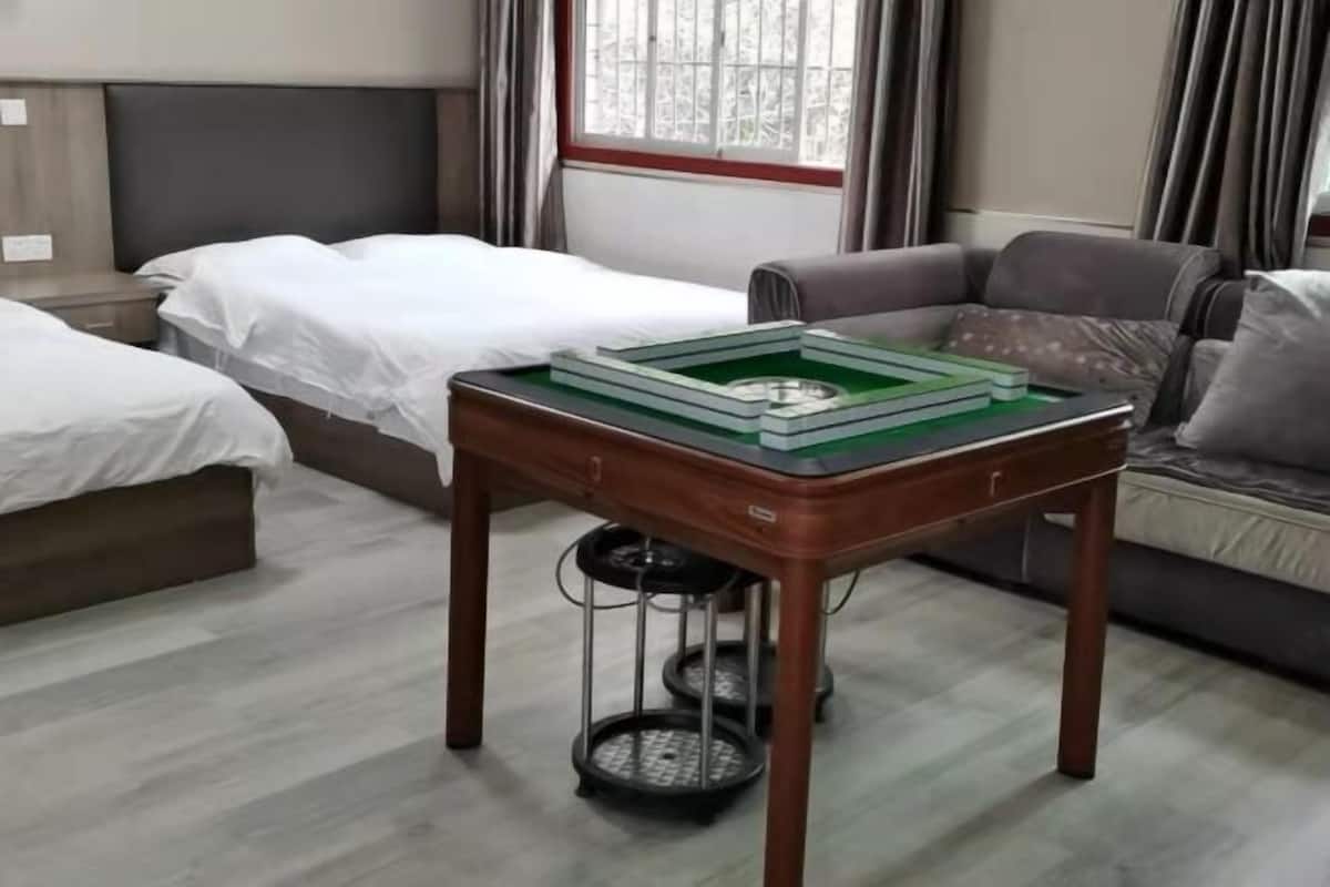 A hotel room with a bed, a sofa, a wooden table with a green tray, and a window with curtains.