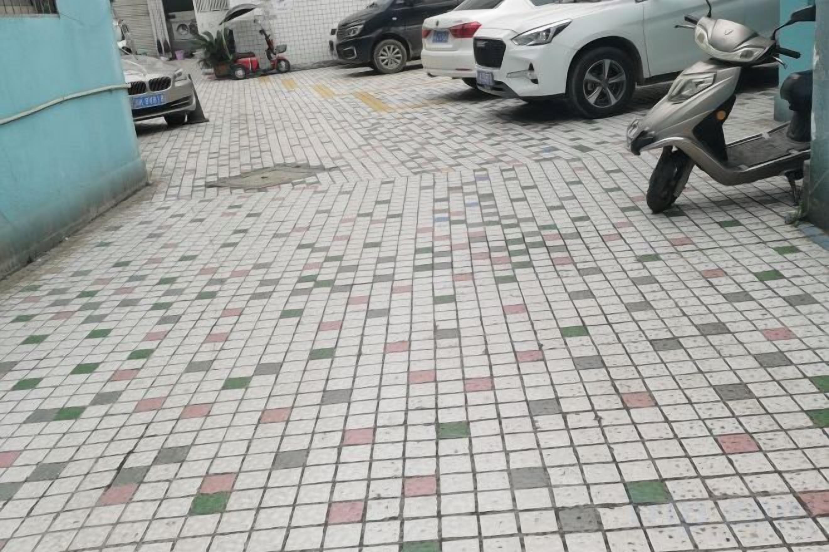 A tiled parking area with a scooter and a white car parked.