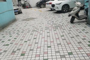 Un estacionamiento con baldosas, con una scooter y un coche blanco aparcados.