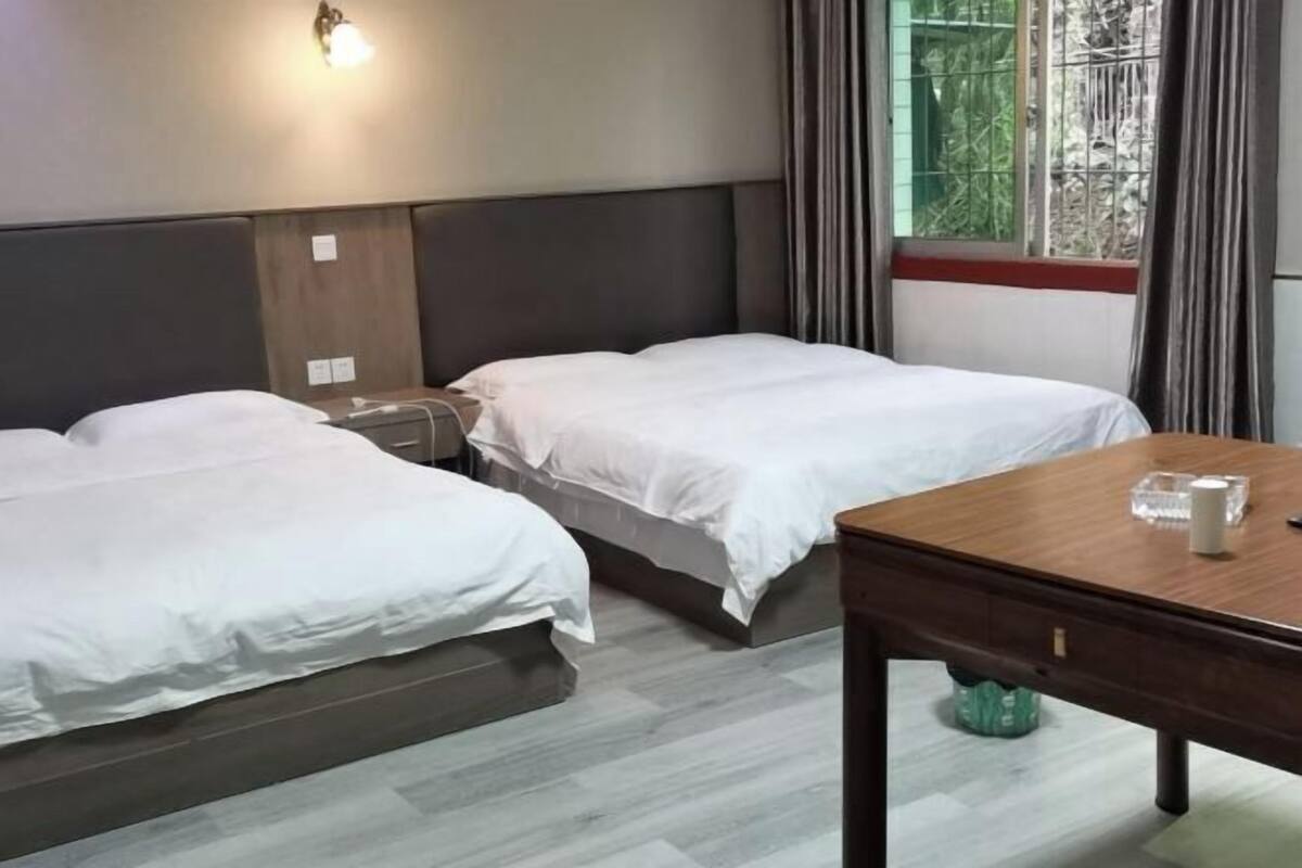 A hotel room with two beds, a wooden table, and a window with curtains.