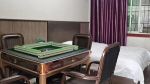 Habitación de hotel con cama, escritorio con un juego de mesa verde, dos sillas y una ventana con cortinas moradas.
