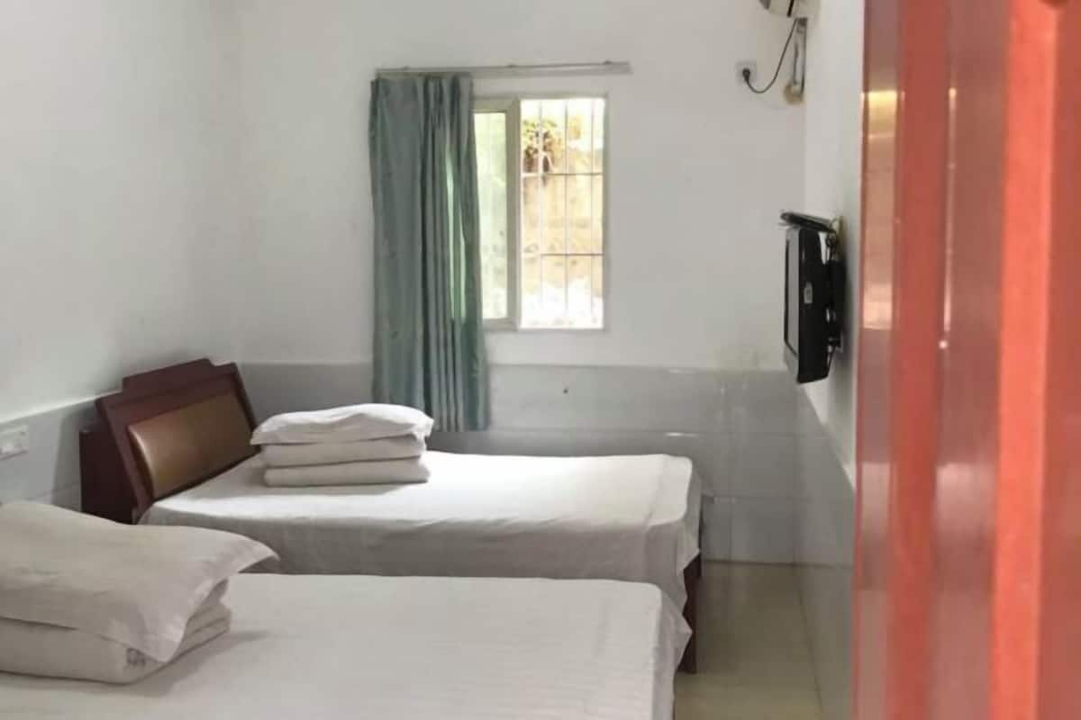 A room with two beds, a window with curtains, a television, and a red door.