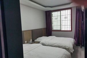 Una habitación de hotel con dos camas, una ventana con rejas y cortinas moradas.