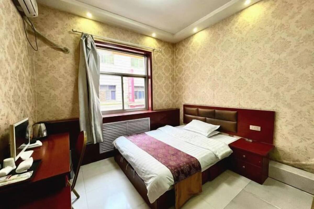 A hotel room with a bed, a desk with a telephone, and a window with curtains.