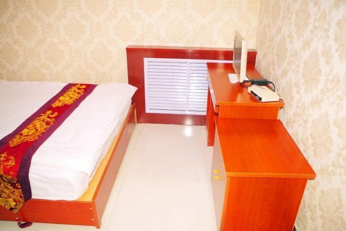 A bedroom with a bed, a desk, a chair, and a window with blinds.