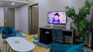 Une pièce comprenant une télévision, un bureau, une chaise, un canapé, une table basse et une plante en pot.
