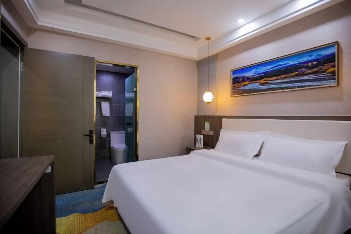 A hotel room with a bed, a nightstand, a painting on the wall, and a door leading to a bathroom.