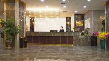 A hotel reception area with a marble counter, a receptionist, and a large screen.