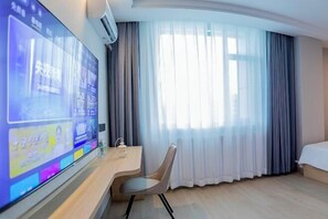 A hotel room with a large flat-screen TV, a desk with a chair, a bed, and a window with sheer curtains. - Dushanzi Hotel (Karamay)