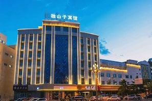 A multi-story hotel with a prominent sign at the top, a large entrance with a canopy, and a parking area in front.