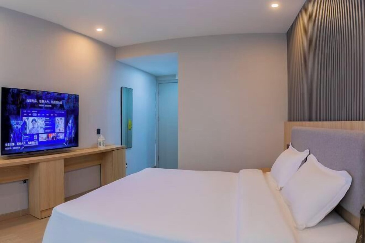 A modern hotel room with a bed, a desk with a flat-screen TV, a mirror, and a wall with vertical lines.