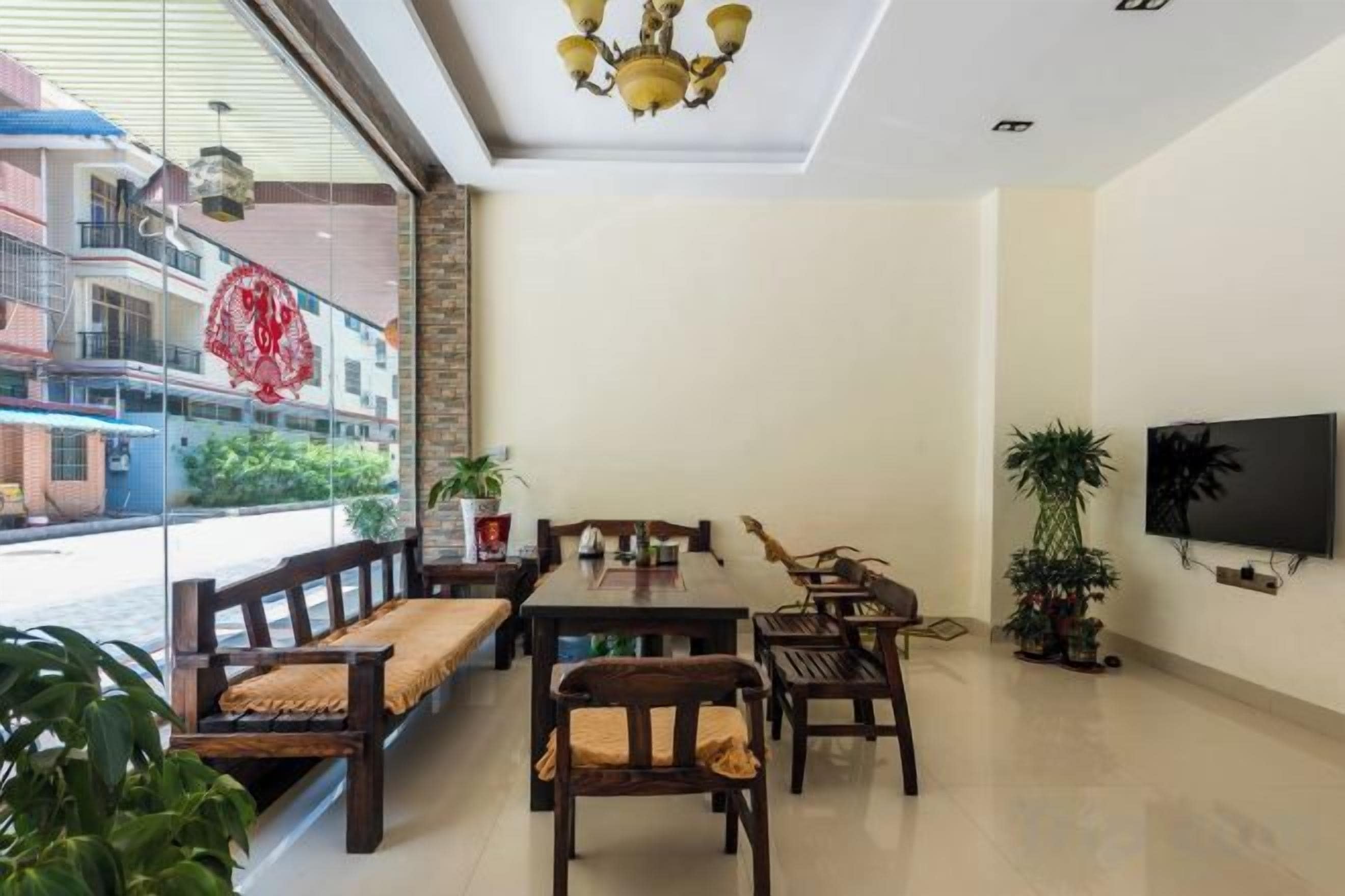 A dining area with a long table and multiple chairs, a TV mounted on the wall, and a balcony with a view of buildings.