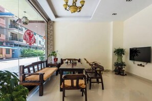 A dining area with a long table and multiple chairs, a TV mounted on the wall, and a balcony with a view of buildings. - The story of Danxia Inn (Renhua)