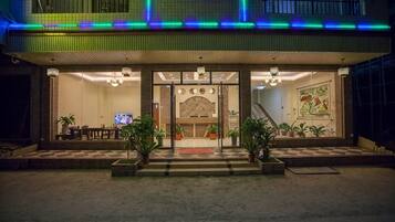 A hotel entrance with a reception desk, a television, and a staircase leading to the upper floor.