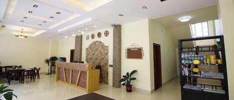 A hotel lobby with a reception desk, seating area, and a bookshelf.
