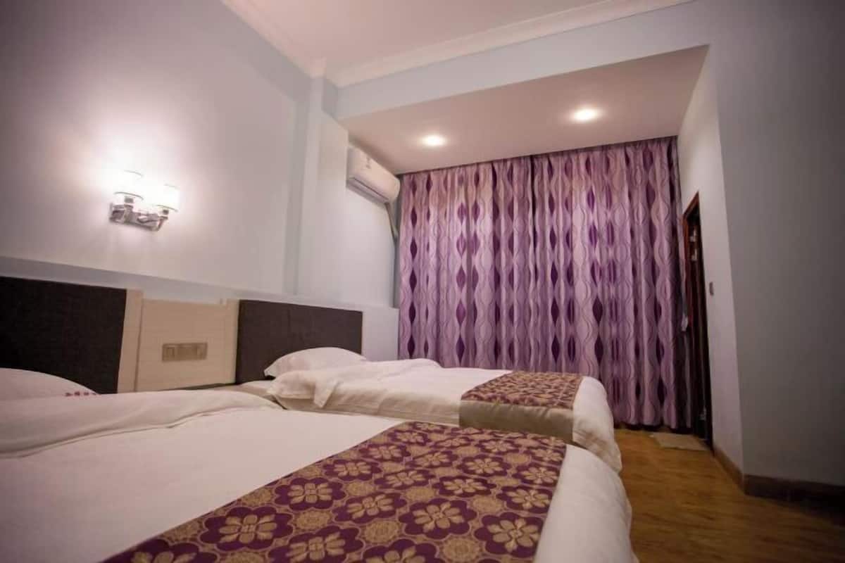 Een hotelkamer met twee bedden, een wandlamp, een airconditioningsunit en een kamerbreed gordijn.