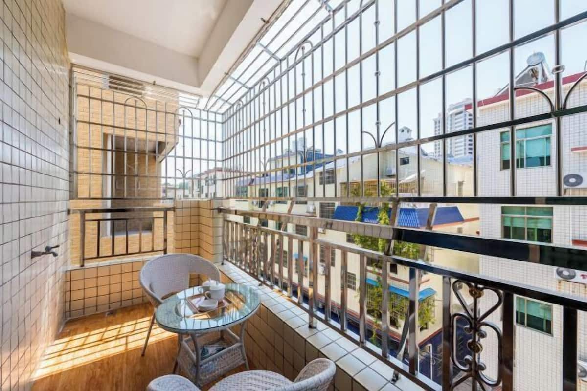 Een balkon met een glazen tafel en stoelen, metalen hekwerk en uitzicht op omliggende gebouwen.