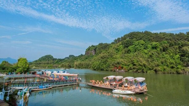 A riverside dock with boats, a pier with a restaurant, and a forested hill in the background. - The story of Danxia Inn (Renhua)