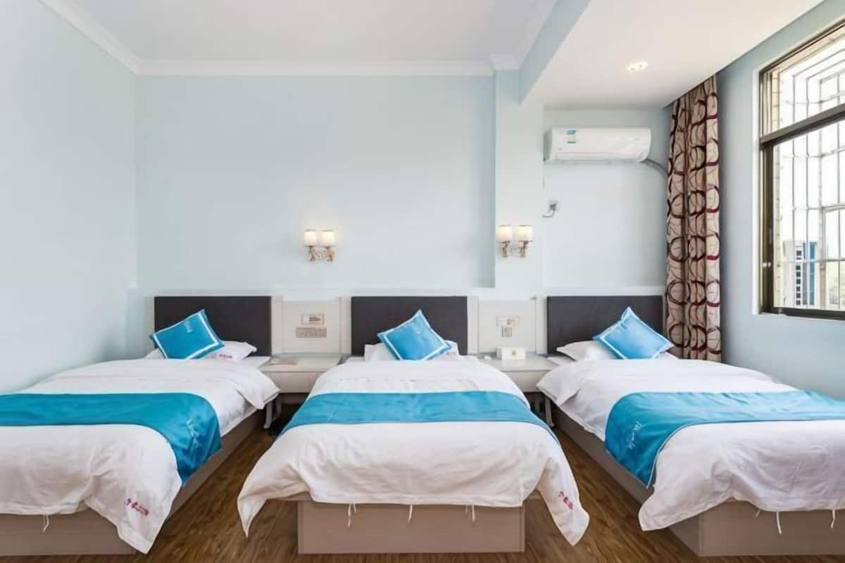 Een hotelkamer met drie bedden, een groot raam met uitzicht en een wandairconditioner.