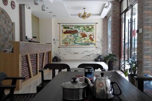 A restaurant interior with a long dining table, chairs, a mural on the wall, and a brick wall. - The story of Danxia Inn (Renhua)