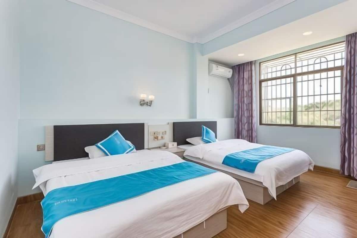 Een hotelkamer met twee bedden, lichtblauwe wanden, een raam met gordijnen en een airconditioning.