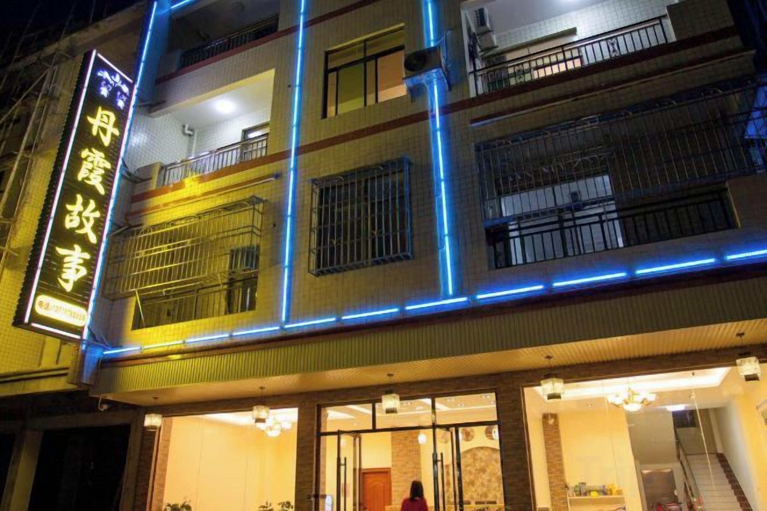 A multi-story building with a prominent neon sign, balconies, and a well-lit entrance.