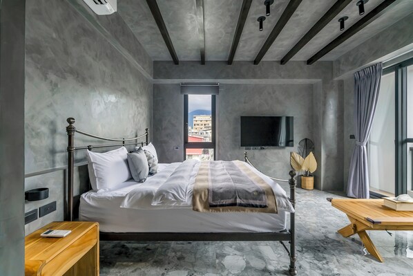Un dormitorio moderno con una cama grande, una mesita de noche de madera, un televisor montado en la pared y vistas de la ciudad a través de una ventana.