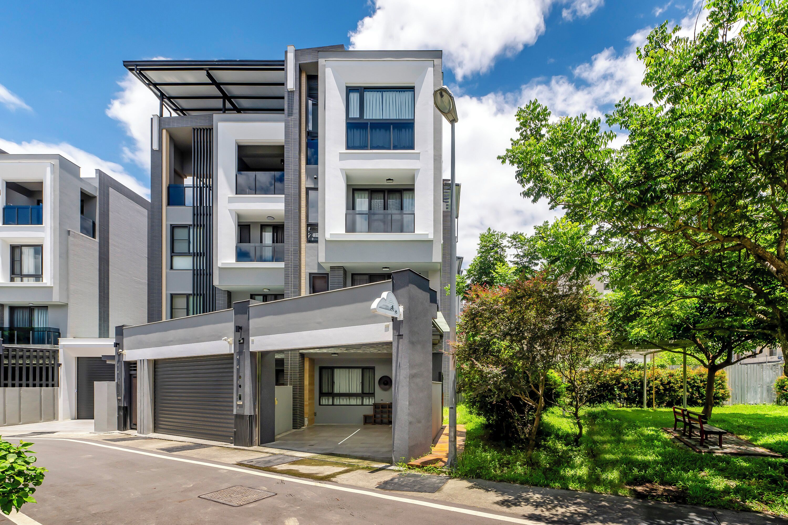 Un edificio residencial moderno de varios pisos con garaje, un área exterior cubierta y un jardín bien cuidado.
