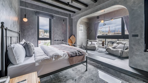 A modern bedroom with a bed, bedside table, and a view of the city through large windows. - Rolling Hills (Puli)