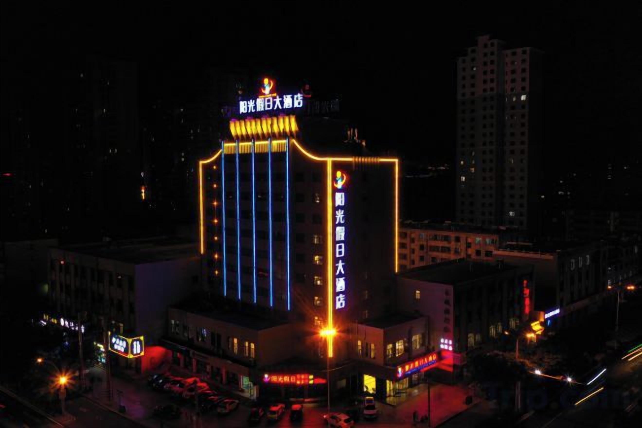 A multi-story building with illuminated signage, a prominent entrance, and a parking area.