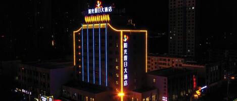 Un edificio de varios pisos con letreros iluminados, una entrada destacada y un área de estacionamiento.