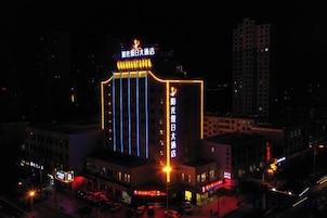 Un edificio de varios pisos con letreros iluminados, una entrada destacada y un área de estacionamiento.